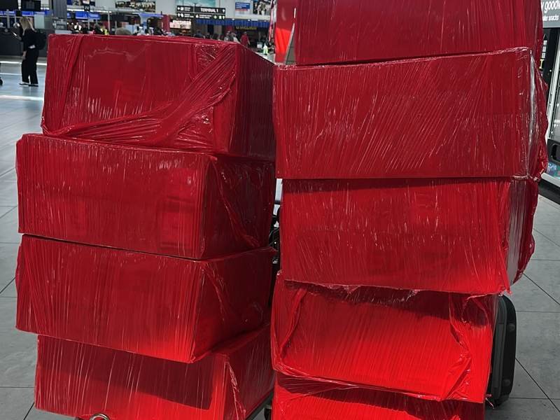 Red shrink-wrapped OBC shipment boxes on airport trolleys